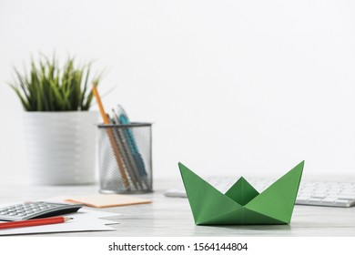 Wooden Office Desk With Green Origami Boat. Individual Investment And Money Saving. Flat Lay Office Workplace With Plant In Pot, Computer Keyboard And Calculator. Green Technologies And Innovations