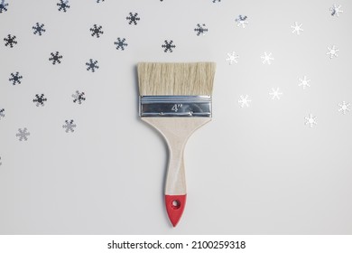 Wooden paint brush on gray with silver snowflakes background. Top view. Winter repairing concept