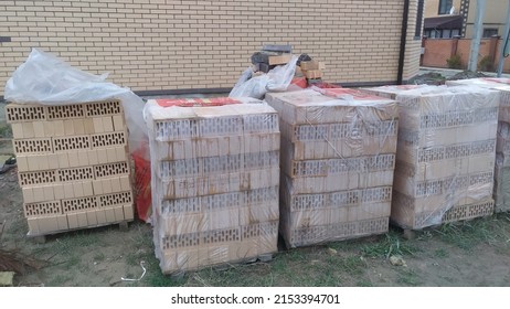 Wooden pallets with hollow bricks wrapped in polyethylene film stand on the grass near the cottage under construction