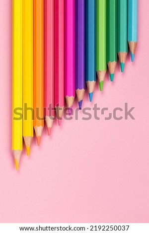 Wooden pastel colored rainbow colors pencils close-up on pink paper background, top view vertical arrangement. The concept of back to school, an example screensaver for a drawing studio for children.