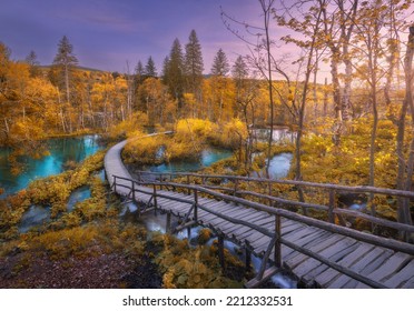 Wooden Path In Orange Forest In Plitvice Lakes, Croatia At Sunset In Autumn. Colorful Landscape With Stairs In Park, Trees, Red Foliage, Water Lilies, River, Pink Sky In Fall. Trail In Woods. Nature