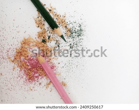 Wooden pencil color shavings and colorful crumbs from sharpener on soft pink pastel and green color. Top view, white background.