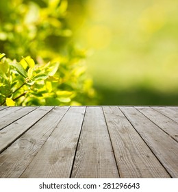 Wooden perspective floor with planks on blurred natural summer background, can use for display or montage your products template. Green forest with ray of light and bokeh. Copy space