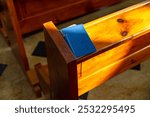 Wooden pew in a church. There is a hymnal book on the pew. The pew is next to a second pew in the background. Both pews are made of wood.