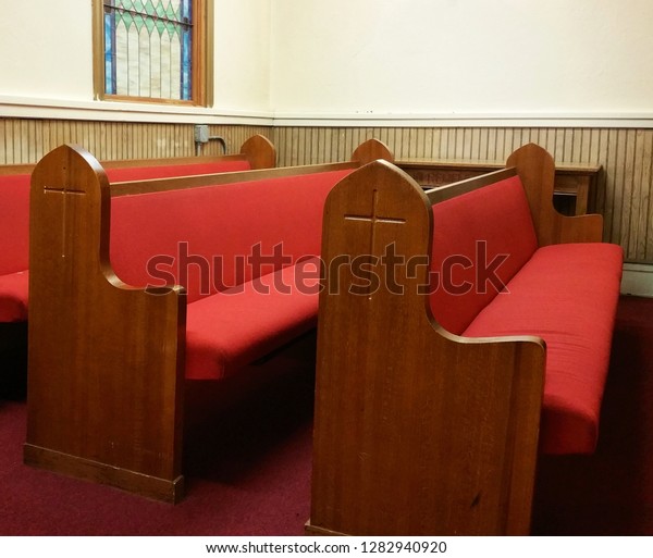 Wooden pews with red cushions; crosses carved on\
the sides.  Pews located in front, left corner of a church in\
Baltimore.  Burgundy carpet.  Wood paneling.  Cream-colored walls. \
Stained glass window.