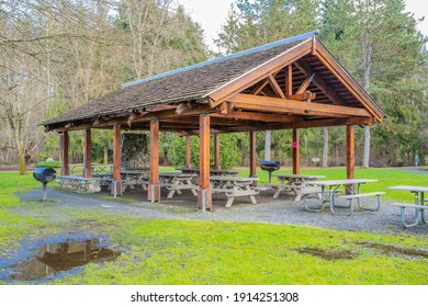 A WOODEN PICNIC SHELTER IN A LOCAL PARK WITH NUMEROUS PICNIC BENCHES