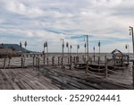 Wooden pier extending into calm body of water in fishing village Ham Ninh, Phu Quoc island, Vietnam, South East Asia. Weathered Pier is lined with rope railings, old pulleys and hanging light bulbs