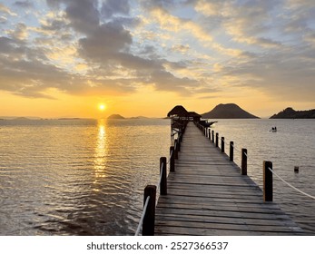 Wooden pier extending towards the horizon with a stunning sunset and golden light reflecting on the calm water. Perfect for travel, vacation and relaxing - Powered by Shutterstock