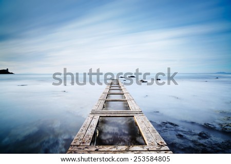 Wooden pier or jetty and rocks on a blue ocean in the morning. Long Exposure