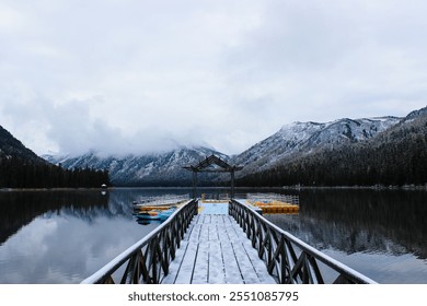 Wooden pier with kayaks on mountain lake in winter with snow covered peaks and reflection creating serene wilderness landscape - Powered by Shutterstock