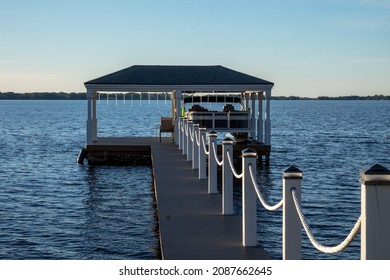 A wooden pier with a large square hut at the wharf. The platform marina has a wooden rail around the wharf and a metal roof. The gazebo stage is over a blue calm ocean. The sky is blue with some cloud