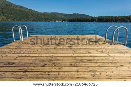 Wooden pier with metal ladder into the sea, lake, water. Swimming dock pier with metal ladder on calm blue lake at sunny day on idyllic resort at Cultus Lake BC