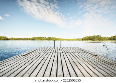 Wooden pier near the river (lake). Evergreen trees in the background. Clear blue sky, reflections on the water. Idyllic summer landscape. Ecotourism, recreation, ecological resort, spa, sauna. Finland - Powered by Shutterstock