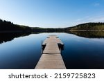 Wooden pier on a calm Lake with reflection in water on a sunny day in early summer. Merrasjärvi, Lahti, Finland.