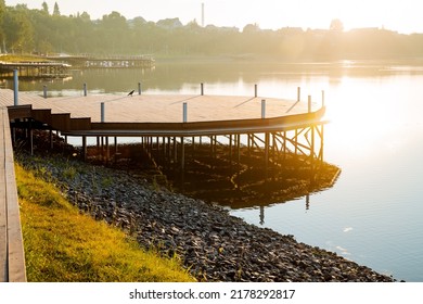 Wooden Pier Stands On The Water, Round Pier, City Park By The Water, Pond For Relaxation, Meditation Area, Morning Light Rays Of The Sun, No People. High Quality Photo