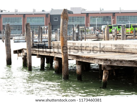 wooden pier supported in piles to embark tourist in Venice, in the background three green buses with a group of people and boats
