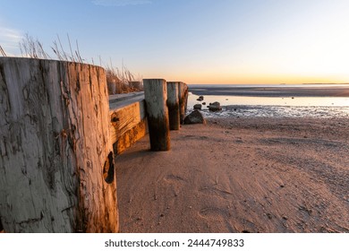 A wooden pier with a wooden walkway leading to the beach. The pier is surrounded by water and sand - Powered by Shutterstock