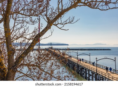 Wooden pier at White Rock, BC extends diagonally into image. Beach and pier at sunset, Surrey, BC, Canada-February 22,2022-Travel photo, selective focus