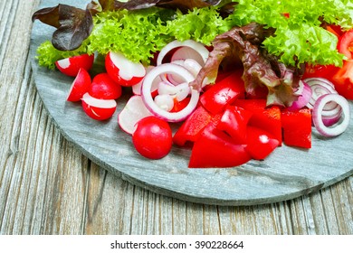 Wooden plate with mixed ingredients for fresh vegetable salad on wooden background