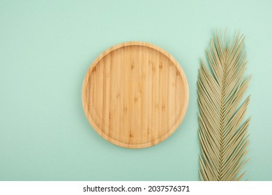 Wooden plate for product presentation with palm leaf. Mockup background with podium and copy space. Empty cylindrical platform for cosmetic. Top view on light mint green background. Skincare cosmetic.