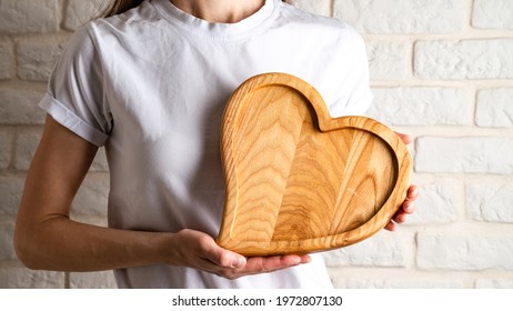 Wooden plate in shape of heart, Heart shaped wooden plate in female hands, empty wooden heart tray in women's hands with copy space for design or text