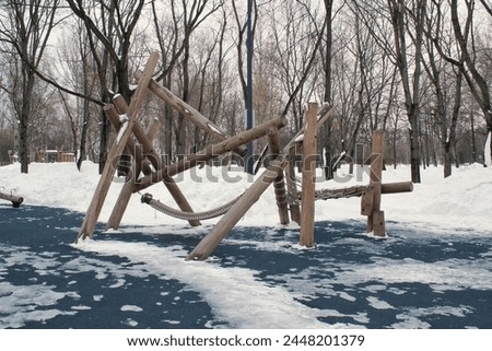 Wooden playground made of natural eco-friendly material in public city park with snow at winter time. Modern safety children outdoor equipment. Winter activities. Children rest and games on open air