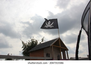 Wooden playhouse for children in the summer garden with a hanging pirate flag.