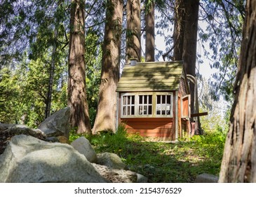Wooden playhouse made of wood. Brown small house between large trees. Wooden fairytale treehouse, playing house on children playground. Nobody, travel photo, selective focus