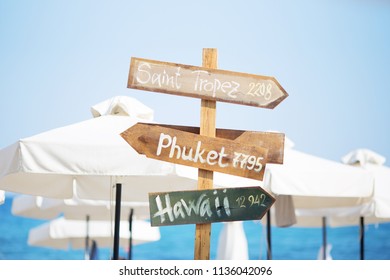 Wooden pointer post with copy space at the beach. arrows on a guidepost pointing at the sea. Signpost showing the way to the beach resorts in front of white umbrellas