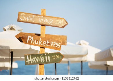 Wooden pointer post with copy space at the beach. arrows on a guidepost pointing at the sea. Signpost showing the way to the beach resorts in front of white umbrellas