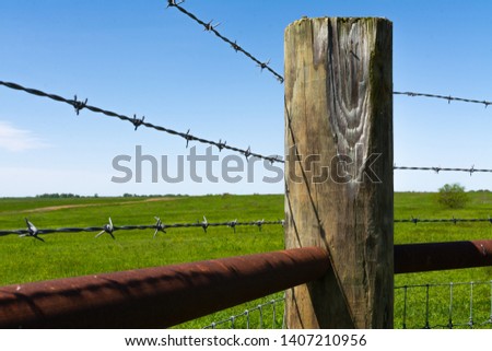 Wooden post and barbed wire with prairie and blue skies in the background.