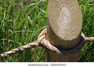 wooden post with brown rustic rope fence in summer outside with green grass and sunlight brightly lit outdoor border - Powered by Shutterstock