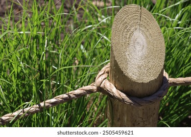 wooden post with brown rustic rope fence in summer outside with green grass and sunlight brightly lit outdoor border - Powered by Shutterstock