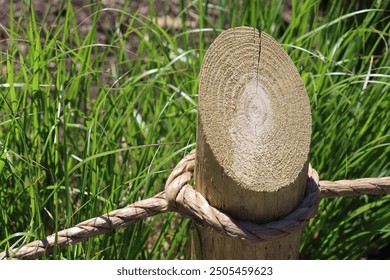 wooden post with brown rustic rope fence in summer outside with green grass and sunlight brightly lit outdoor border - Powered by Shutterstock