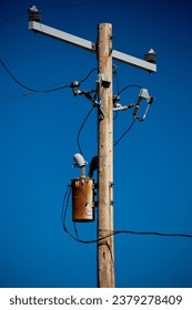 Wooden Power Pole with Rusty Distribution Transfromer with Metal Crossarm on dark blue cloudless sky