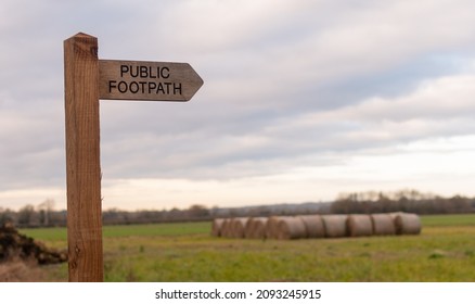 Wooden Public Footpath Sign With Blurred Hay Bales In Background, UK Countryside Scene