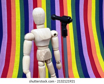 Wooden puppet standing in front of a rainbow background and addressing a microphone; LGBT and diversity concept.