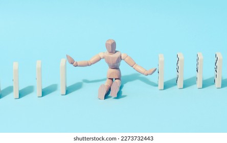 A wooden puppet toy holds back a falling domino on a blue background, representing the concept of a strong personality - Shutterstock ID 2273732443