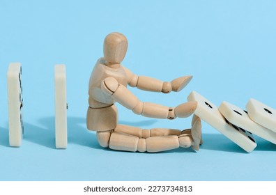 A wooden puppet toy holds back a falling domino on a blue background, representing the concept of a strong personality - Shutterstock ID 2273734813