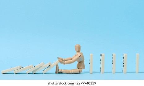 A wooden puppet toy holds back a falling domino on a blue background, representing the concept of a strong personality - Shutterstock ID 2279940119