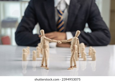 Wooden puppets hold hands and business people sit in the background. Business deals and leaders shake hands. - Powered by Shutterstock