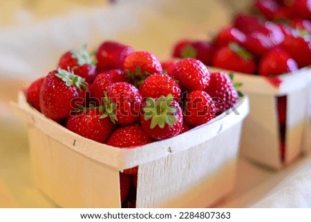 Wooden quart containers of fresh red, ripe strawberries with the stems still on them. The packages are in a row on a grocery store shelf.  The berries are firm, rich, and vibrant with green stems.