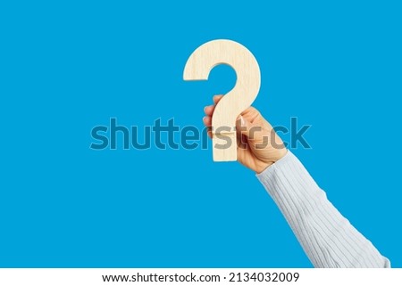 Wooden question mark in human hand on empty blue background. FAQ, asking question, being unsure, seeking truth, guessing, unclear answer, mystery, secret, riddle, confusion, exam, consultation concept