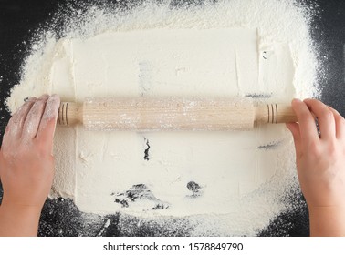 wooden rolling pin in female hands on a black background with white wheat flour, top view - Powered by Shutterstock