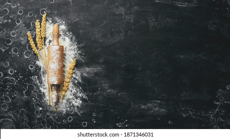 Wooden rolling pin and flour. Bakery on a black stone background. Top view. Free space for text.