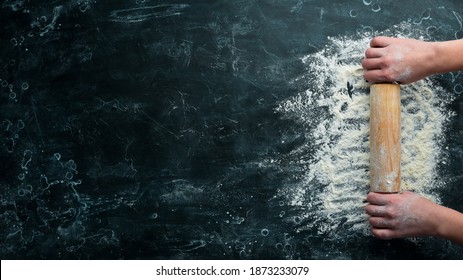 Wooden rolling pin in hands and flour. Bakery on a black stone background. Top view. Free space for text. - Shutterstock ID 1873233079