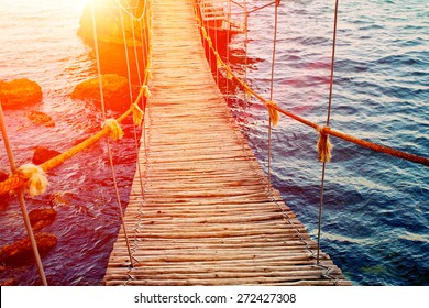 Wooden Rope Bridge Over Rocky Sea Coast At Sunset