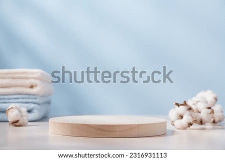 Wooden round podium pedestal. Product presentation  on blue background with cotton towels and branch of cotton