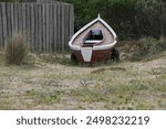 Wooden rowboat on sandy beach with grass and wooden fence in background