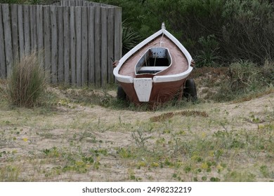 Wooden rowboat on sandy beach with grass and wooden fence in background - Powered by Shutterstock